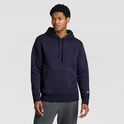 A man wearing the Champion Powerblend Hoodie, C Logo in navy blue stands against a plain light gray background. He has short curly hair, is dressed in dark gray sweatpants, and looks slightly to the side with a neutral expression.