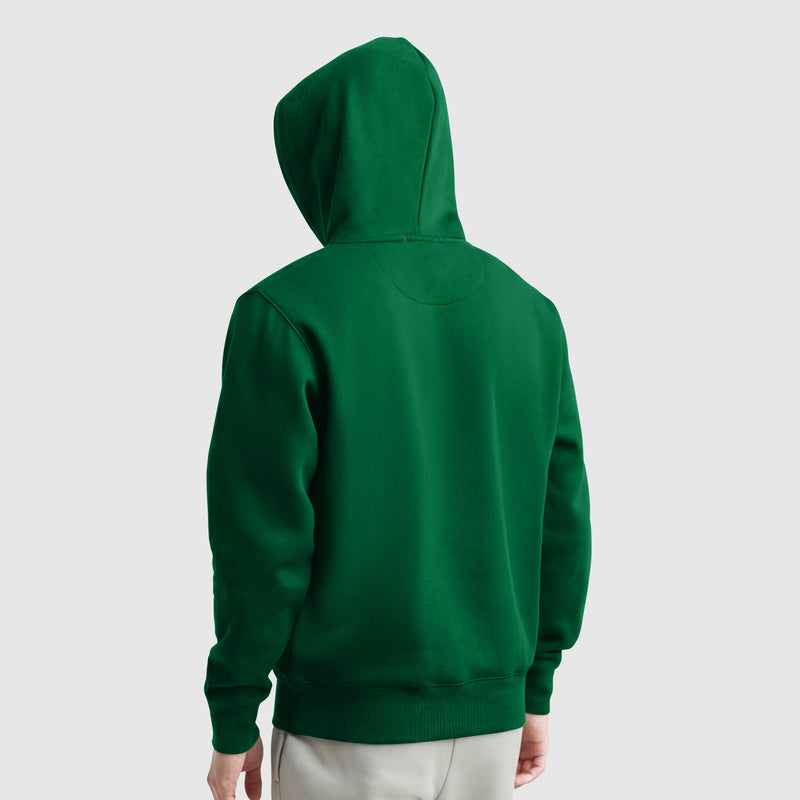 A person wearing a green Champion Powerblend Hoodie, C Logo, with the hood up, seen from the back against a plain light gray background.