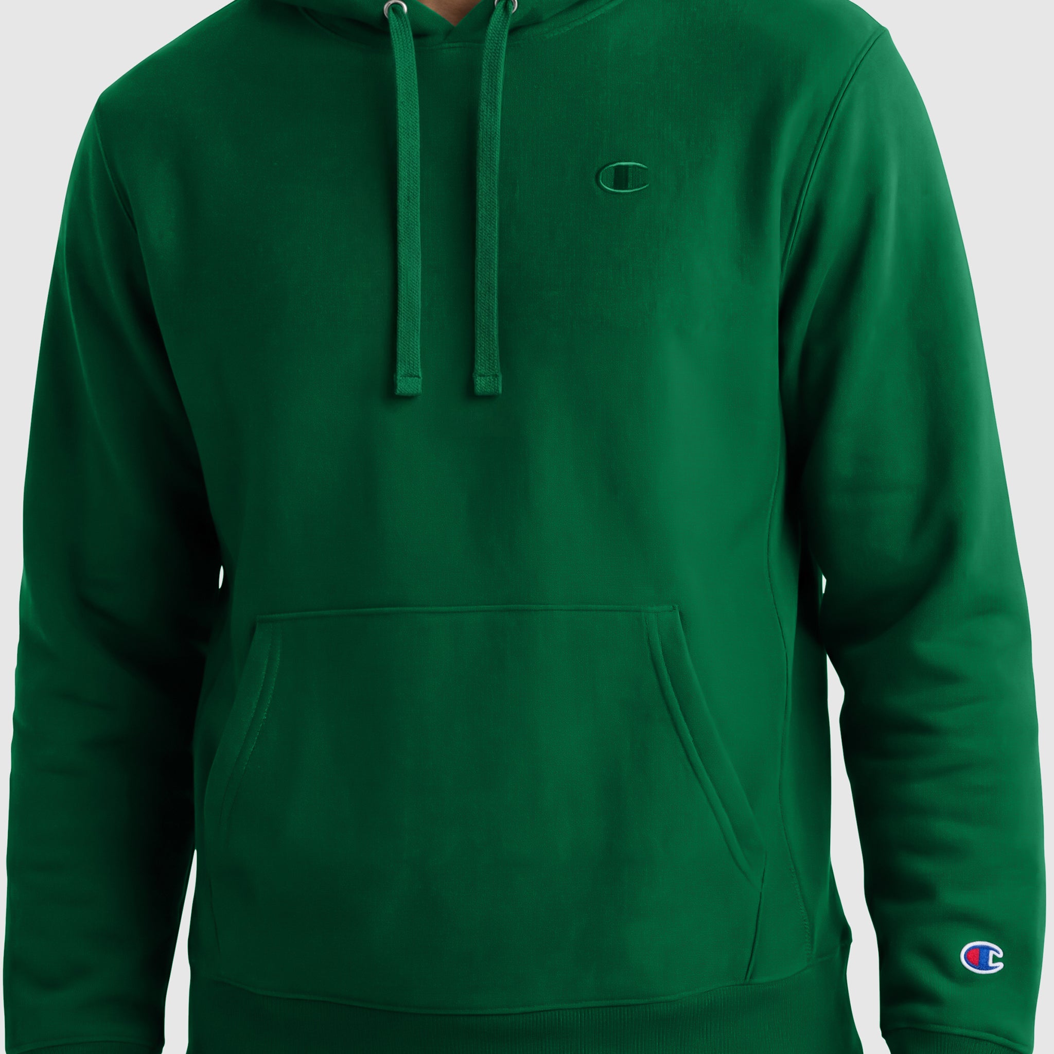 A person wears a plain green Champion Powerblend Hoodie, C Logo, featuring a front pocket, drawstrings, and small Champion logos on the left chest and sleeve. The person's face is not visible.