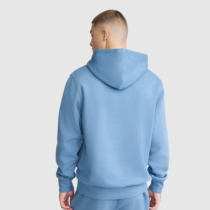 A person wearing a light blue Champion Powerblend Hoodie, C Logo, along with matching sweatpants, is standing with their back to the camera against a plain white background.
