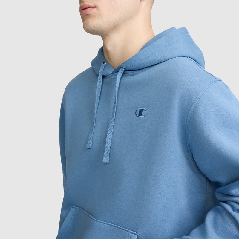 A person is wearing a light blue Champion Powerblend Hoodie, C Logo, with drawstrings visible at the shoulders and chest, standing against a plain light gray background.