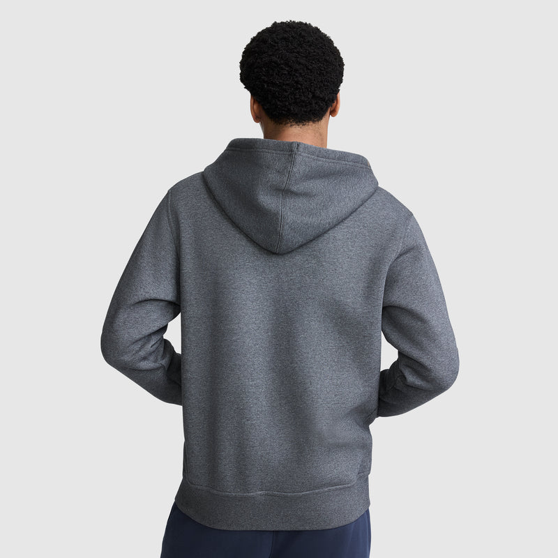 A person stands facing away with hands on hips, wearing a Champion Powerblend Full-Zip Hoodie, C Logo in dark gray with the hood down, paired with fleece sweatpants against a plain light gray background.