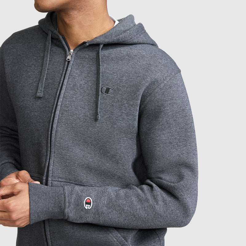 A person wearing the Champion Powerblend Full-Zip Hoodie, C Logo in gray stands against a plain light gray background, paired with Champion men's sweatpants crafted from soft brushed fleece.