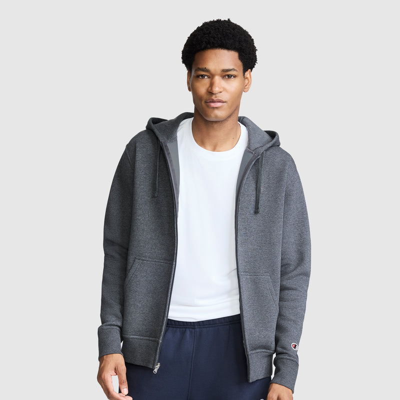 A man wearing a Champion Powerblend Full-Zip Hoodie, C Logo in dark gray over a white T-shirt and navy Powerblend cinched bottom fleece sweatpants stands against a plain light gray background.