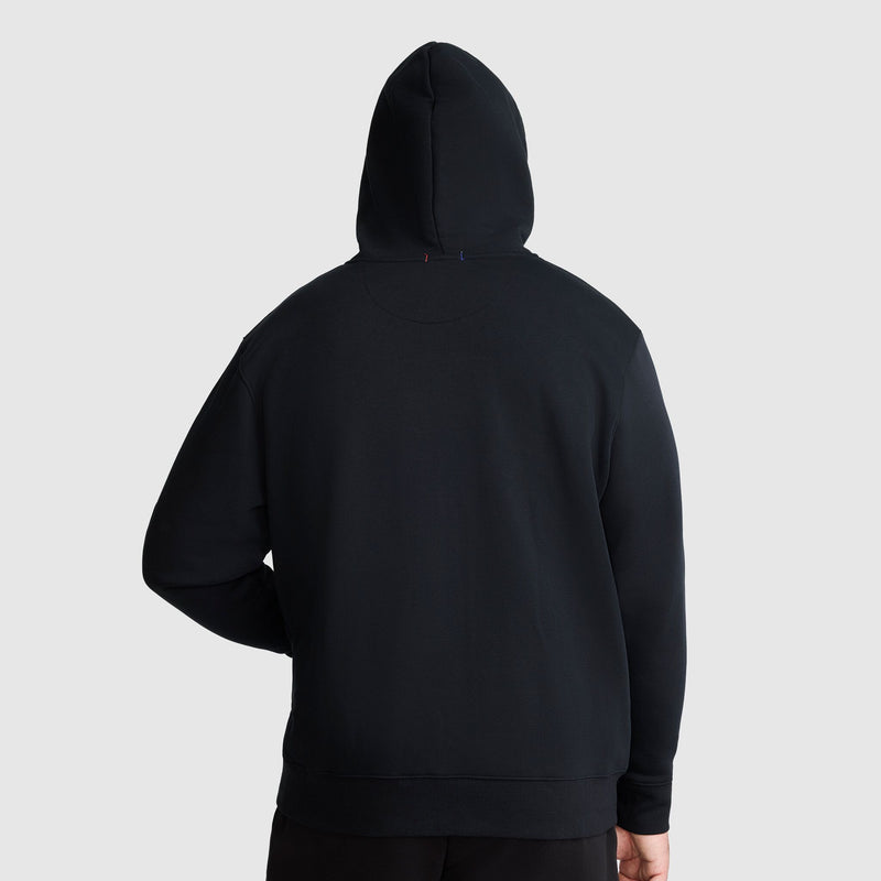 A person wearing a Champion Powerblend Full-Zip Hoodie, C Logo - Big & Tall stands facing away from the camera against a light gray background. The hood is up, covering their head.