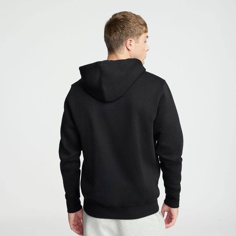 A person wearing a Champion Powerblend Full-Zip Hoodie, C Logo in black and light gray pants stands facing away from the camera against a plain white background.