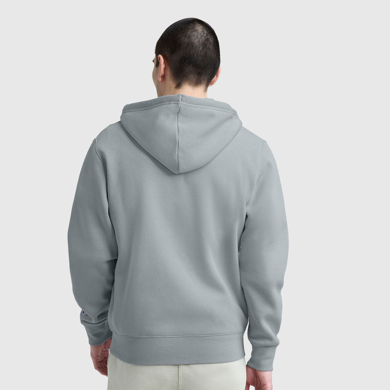 A person with short dark hair, seen from behind, is wearing a light gray Champion Powerblend Full-Zip Hoodie, C Logo, and light-colored pants against a plain light background.