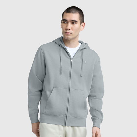 A man with short hair wears the Champion Powerblend Full-Zip Hoodie, C Logo, paired with cream pants, standing against a plain light gray background and looking slightly to the side.