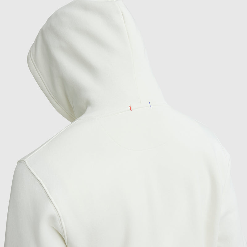 A person wearing a plain white Champion Powerblend Full-Zip Hoodie, shown from the back. The hood is up, revealing small red, white, and blue vertical stitch accents near the neck and a classic C logo detail.