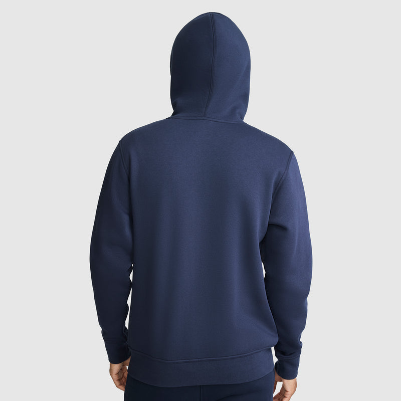A person wearing a navy blue Champion Powerblend Full-Zip Hoodie, C Logo, stands facing away with the zip-up hood up, against a plain light background.
