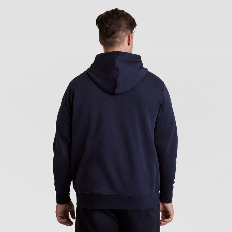 A person wearing a dark blue Champion Powerblend Full-Zip Hoodie, C Logo - Big & Tall stands facing away from the camera against a light gray background.