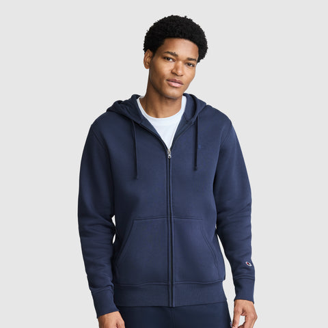 A man is shown facing forward against a plain light gray background, wearing a Champion Powerblend Full-Zip Hoodie, C Logo in navy blue with a hood and drawstrings, paired with matching pants.