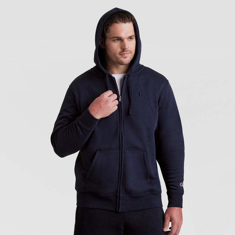 A man wearing a navy blue Champion Powerblend Full-Zip Hoodie, C Logo – Big & Tall, with the hood up over a white t-shirt and paired with black pants, stands against a plain light gray background.
