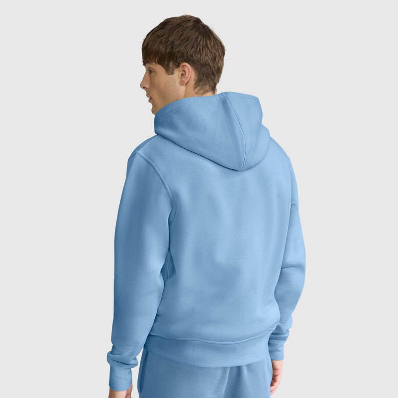 A person with short brown hair is wearing a light blue Champion Powerblend Full-Zip Hoodie, C Logo, paired with matching pants. They are standing and facing away, looking to the left, against a plain light background.