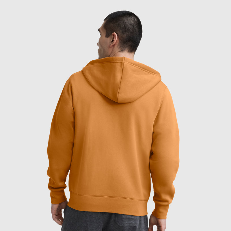 A man stands with his back to the camera, wearing the Champion Powerblend Full-Zip Hoodie, C Logo in orange and dark gray pants against a plain light gray background.