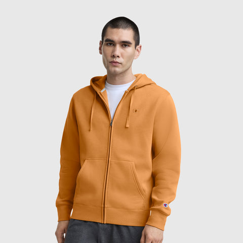 Here’s a rewritten version using your product data: A person stands facing forward against a plain light background, wearing a Champion Powerblend Full-Zip Hoodie with the C Logo in orange over a white T-shirt and gray pants.