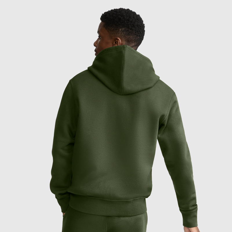 A person wearing an olive green Champion Powerblend Full-Zip Hoodie, C Logo, and matching pants is standing with their back to the camera against a plain, light gray background.