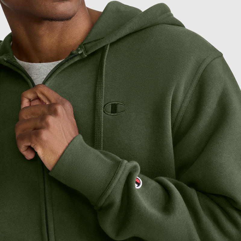 A person zips up the Champion Powerblend Full-Zip Hoodie, C Logo in olive green, displaying both the iconic chest logo and the sleeve patch. With only part of their face visible, the timeless style of this men’s hoodie stands out.