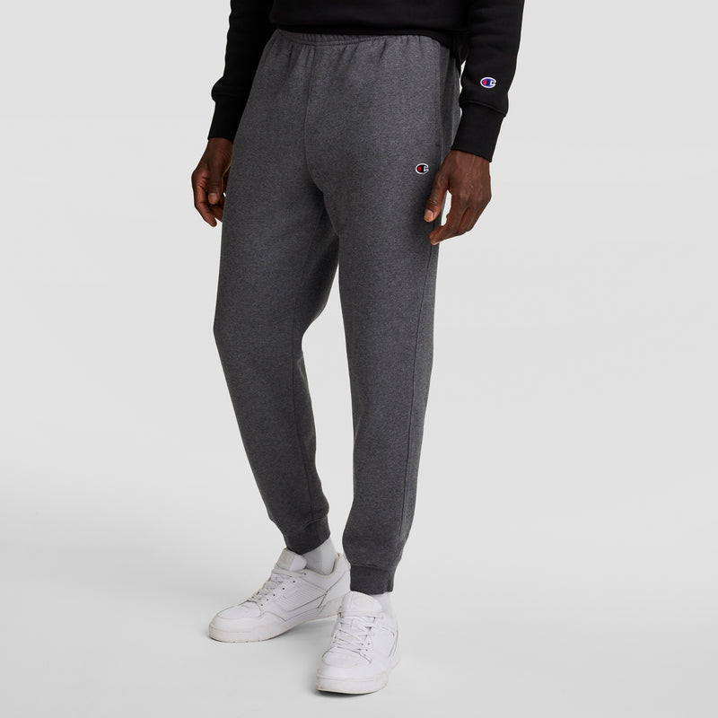 A person wearing Champion Powerblend Joggers, C Logo in dark gray and a black Champion sweatshirt stands against a plain white background. The Champion logo appears on both the joggers and the sweatshirt.