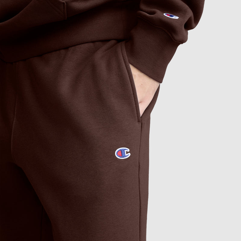 A person wearing Champion’s Powerblend Joggers, C Logo, paired with a matching sweatshirt, rests their hand in the pocket. Both garments feature the Champion logo and are shown against a plain light gray background.