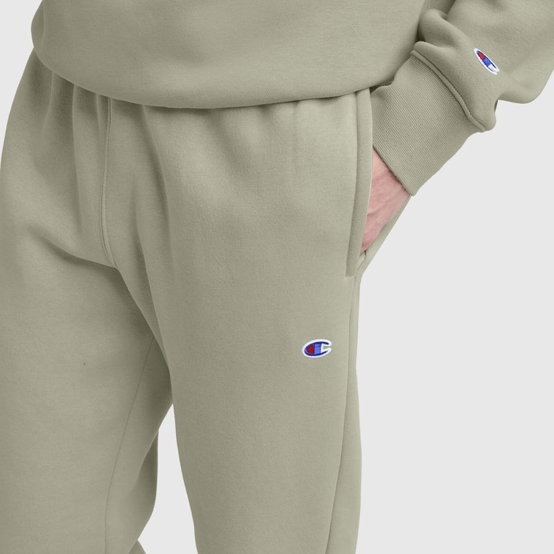 A person wears Champion Powerblend Sweatpants with a cinched bottom and C logo, paired with a matching sweatshirt. The cotton blend outfit is set against a plain white background, with one hand in the pants pocket.