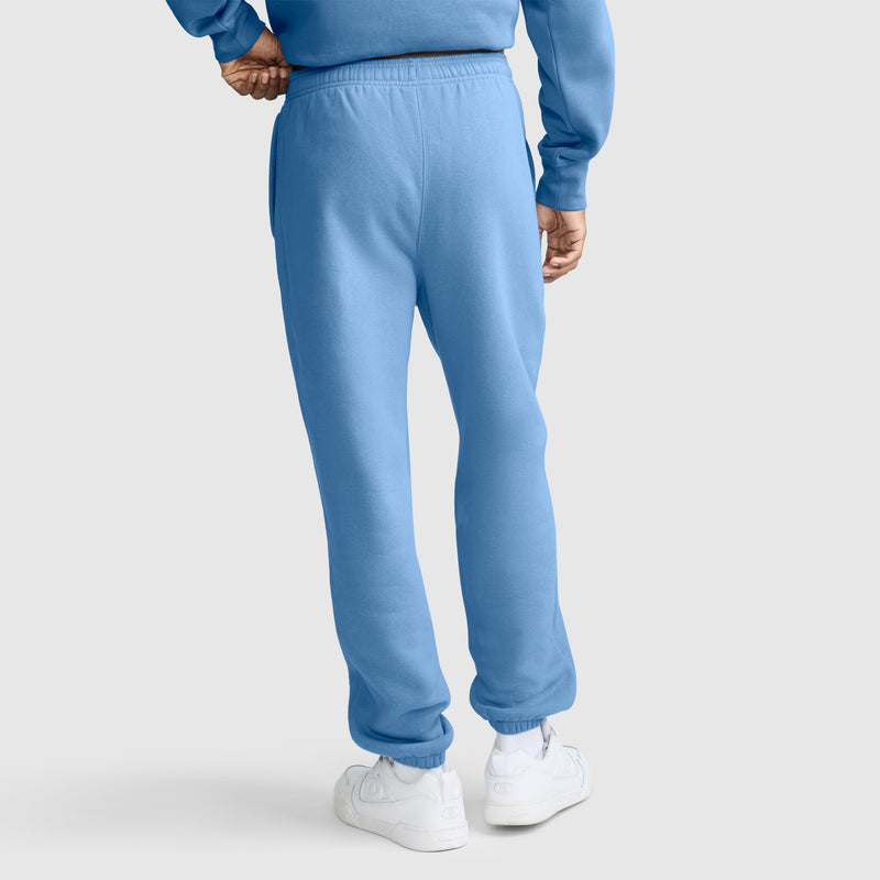 A person wearing the Champion Powerblend Sweatpants, Cinched Bottom, C Logo in light blue along with a matching sweatshirt and white sneakers stands with their back to the camera against a plain light gray background.