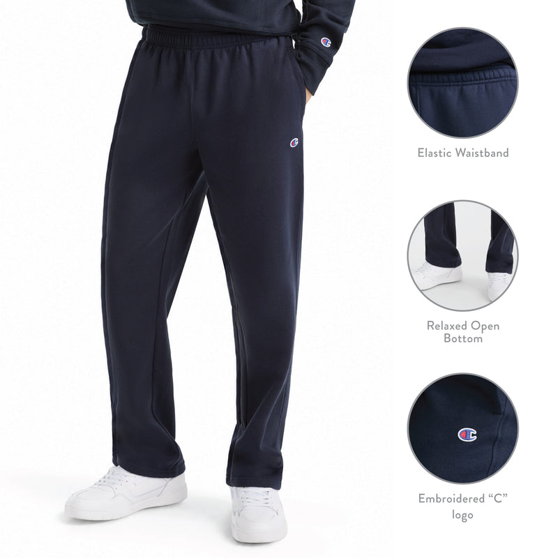 A person is wearing Champion Powerblend Sweatpants, Open Hem, C Logo in navy blue. These men’s sweatpants feature an elastic waistband, relaxed open bottom, and a small embroidered C logo. Crafted from a soft cotton blend for comfort and style, the design includes insets highlighting the waistband, pant hem, and logo details. White sneakers complete the look.