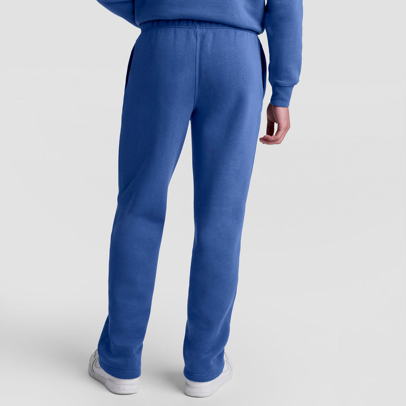 A person faces away, wearing Champion Powerblend Sweatpants, Open Hem, C Logo in blue with a matching blue sweatshirt and white sneakers, set against a light gray background.