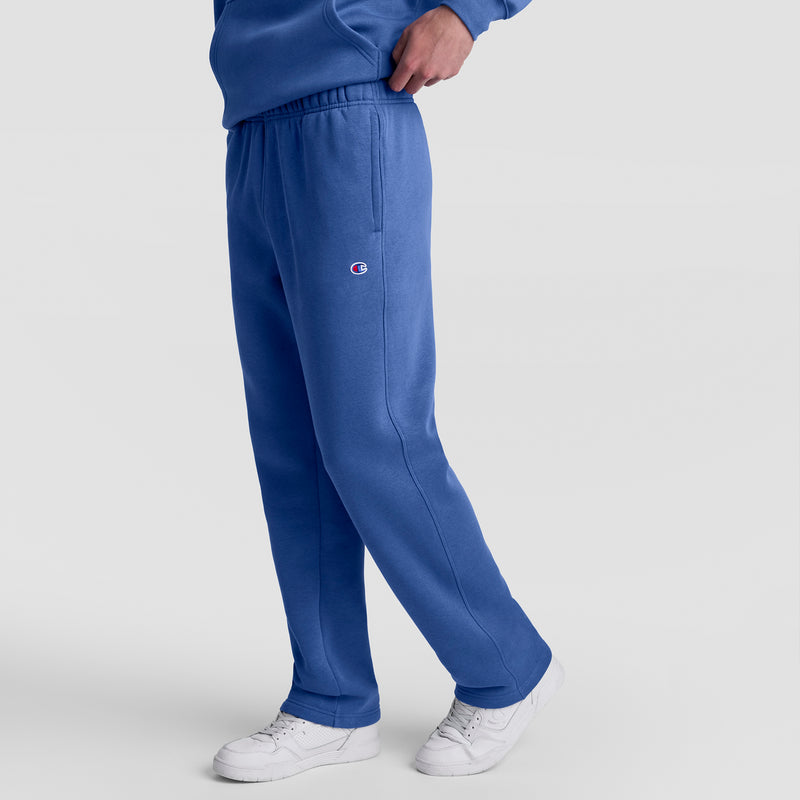 A person wears Champion Powerblend Sweatpants, Open Hem, C Logo in blue with a matching sweatshirt and white sneakers, standing against a light gray background. Only the lower half of the body is shown.