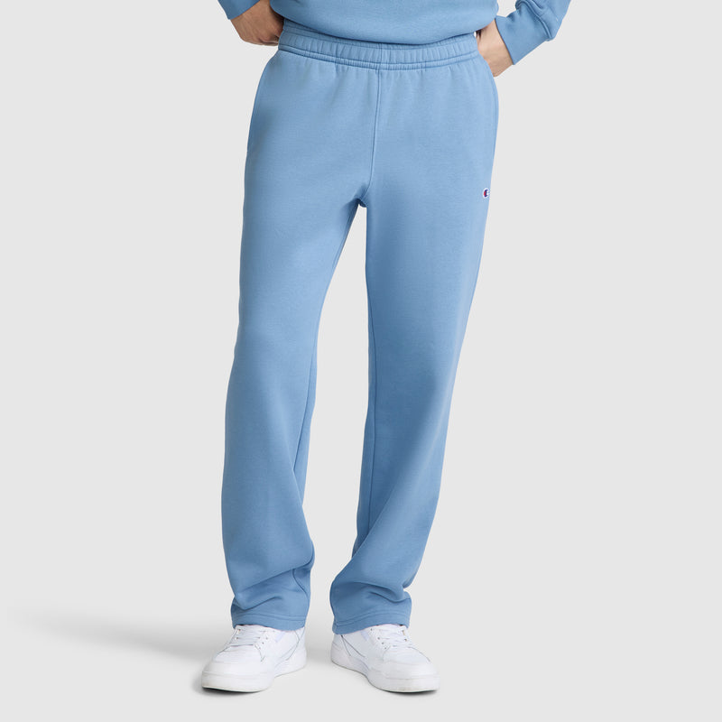 A person wearing light blue Champion Powerblend Sweatpants, Relaxed Bottom, C Logo, along with a matching sweatshirt and white sneakers, stands against a plain background with hands resting on hips.