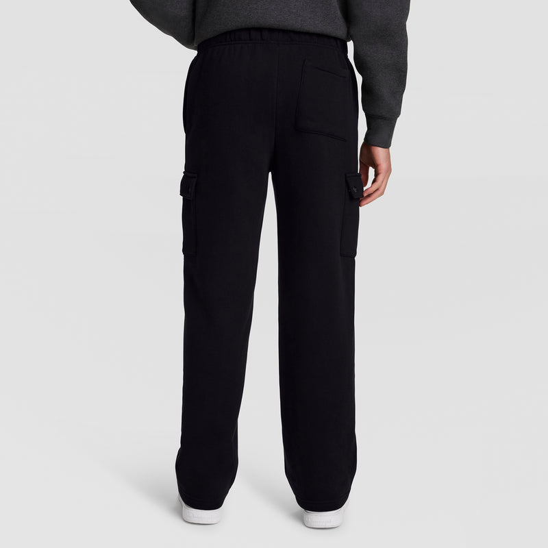 A person is seen from the back wearing Champion’s Fleece Cargo Pant, C Logo, styled with a dark sweatshirt. The black pants feature side and back pockets and are crafted from a comfortable cotton-polyester fleece fabric. The individual is standing on a plain light background.