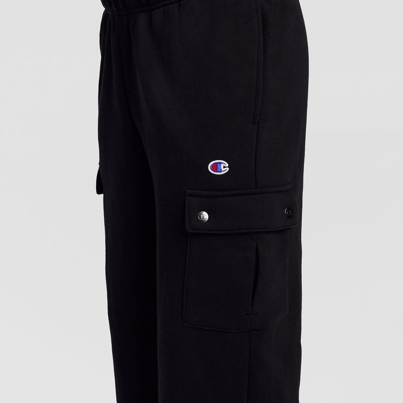 Close-up of the Champion Fleece Cargo Pant, C Logo in black streetwear style, featuring a cargo pocket with snap buttons. The signature Champion C logo patch is displayed above the pocket. The background is plain and light-colored.