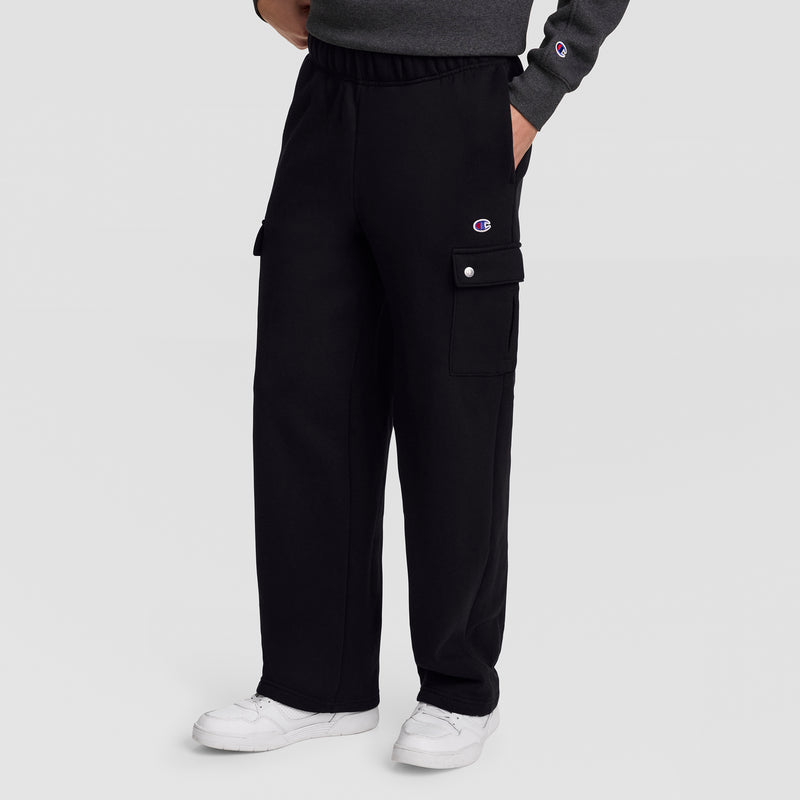 A person wearing Champion Fleece Cargo Pant, C Logo in black streetwear style pairs them with white sneakers, hands in pockets. The pants feature side cargo pockets and a small Champion “C” logo near the waist. Only the lower half is visible, drawing attention to the comfortable cotton-polyester fleece design of these Champion cargo pants.