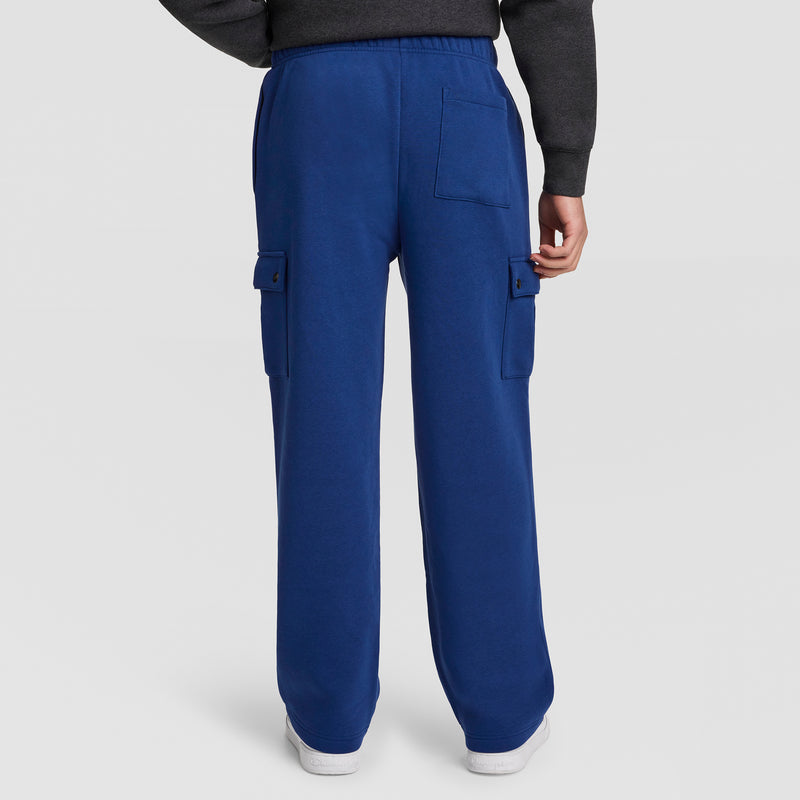 A person is shown from the back, wearing Champion Fleece Cargo Pant with C Logo in royal blue. The men’s streetwear pants feature flap pockets on the sides and back. Only the lower half of the body is visible against a plain white background.