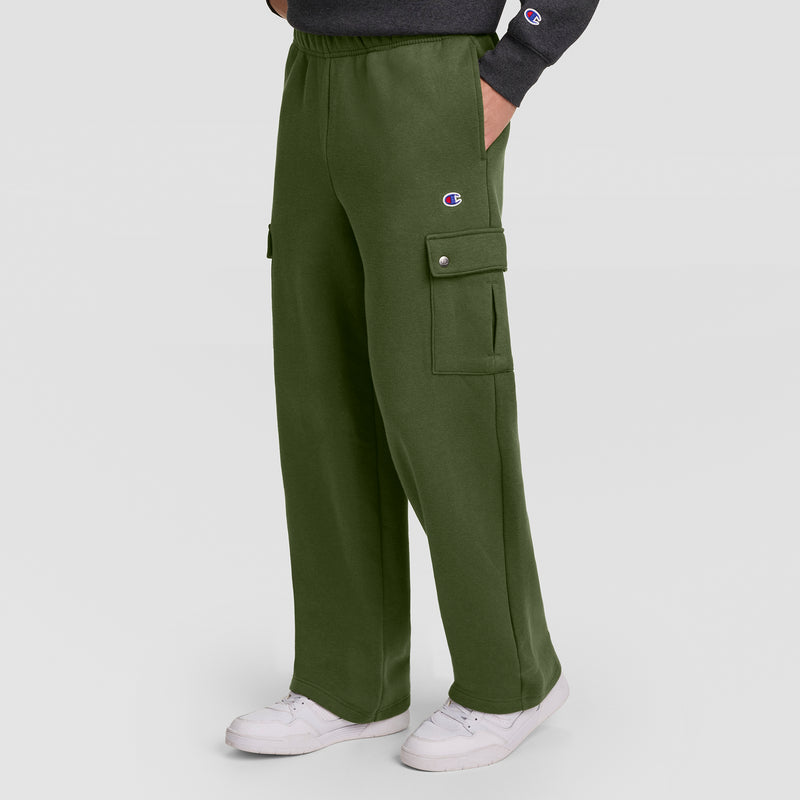 Wearing the Champion Fleece Cargo Pant, C Logo in olive green—designed with practical pockets and a subtle Champion “C” logo on the thigh—this look is styled with a dark sweatshirt and white sneakers, set against a plain light background for an easygoing streetwear vibe.