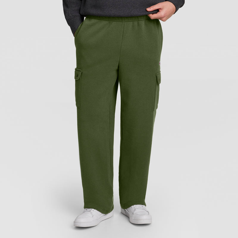 Dressed in Champion’s Fleece Cargo Pant, C Logo—a stylish olive green men’s cargo sweatpant inspired by streetwear—this individual pairs the look with a dark sweatshirt and white sneakers, standing with one hand in a pocket against a plain background.