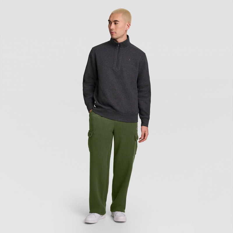 A person with short blond hair wears a dark gray quarter-zip sweater, Champion Fleece Cargo Pant, C Logo in olive green, and white sneakers, standing against a plain white background.