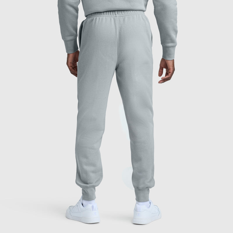 Someone wearing light gray Champion Powerblend Joggers with the Script Logo, a matching sweatshirt, and white sneakers stands with their back to the camera against a plain white background.