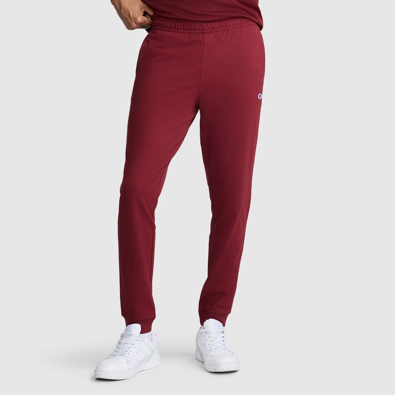 A person is shown from the waist down wearing Champion Lightweight Lounge Joggers, C Logo in maroon and white sneakers, standing against a plain light gray background.