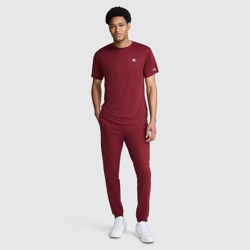 A person stands facing forward, wearing a matching maroon short-sleeve shirt and Champion Lightweight Lounge Joggers with the C Logo, paired with white sneakers, against a plain light gray background.