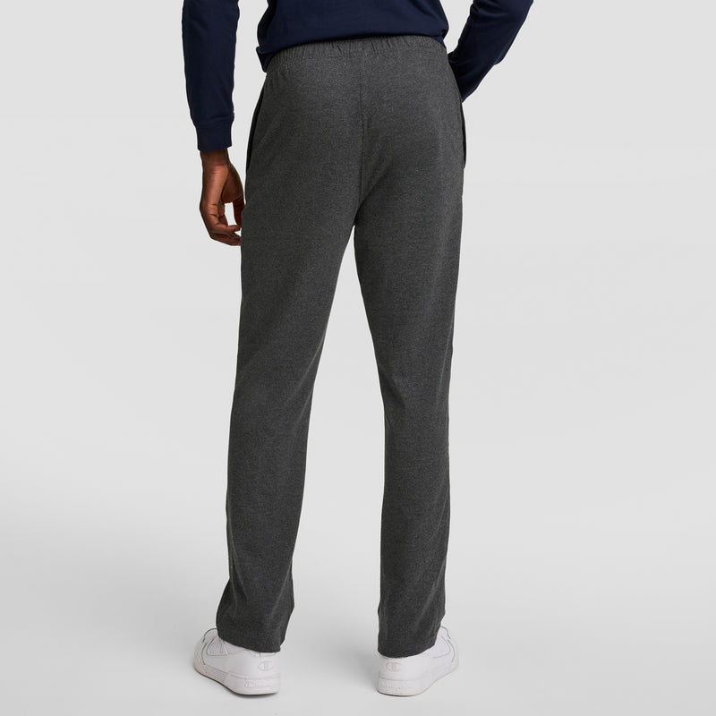 A person stands facing away, wearing Champion Lightweight Lounge Pants with an open hem and C logo, paired with a navy long-sleeve top and white sneakers against a plain light background.