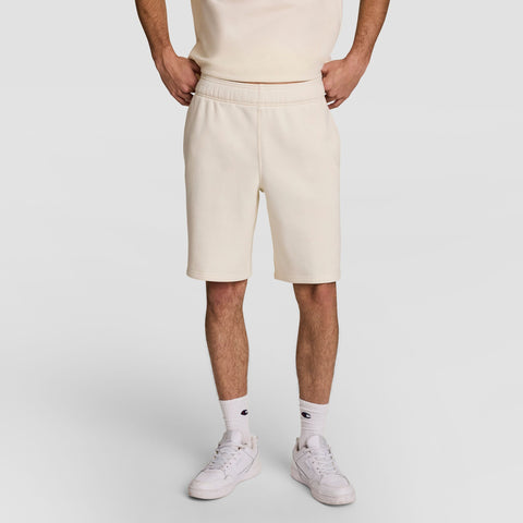 A person stands with hands on hips, wearing a cream-colored T-shirt, matching shorts, white crew socks, and white sneakers, against a plain light background. The persons face is not visible.