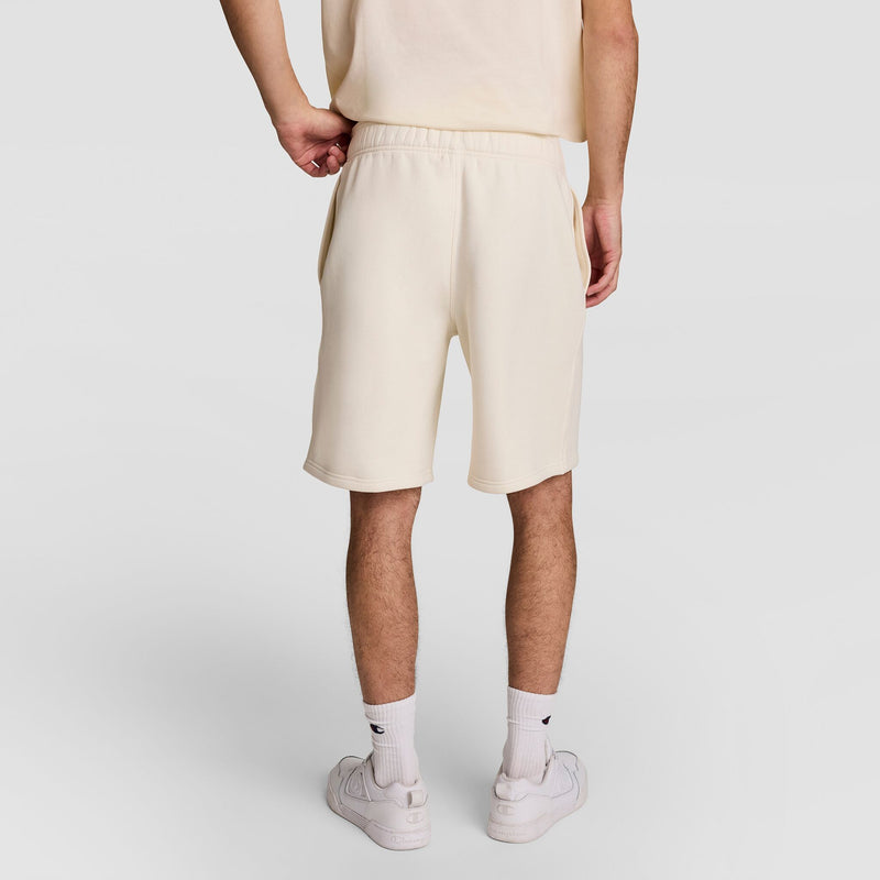 A person stands facing away, wearing a cream-colored T-shirt and matching shorts, white crew socks, and white sneakers against a plain light background.