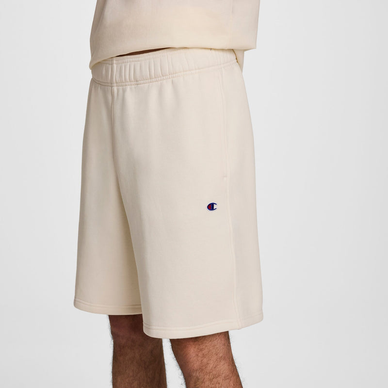 A person wearing light beige shorts with an elastic waistband and a small Champion logo on the left leg, standing against a plain white background.