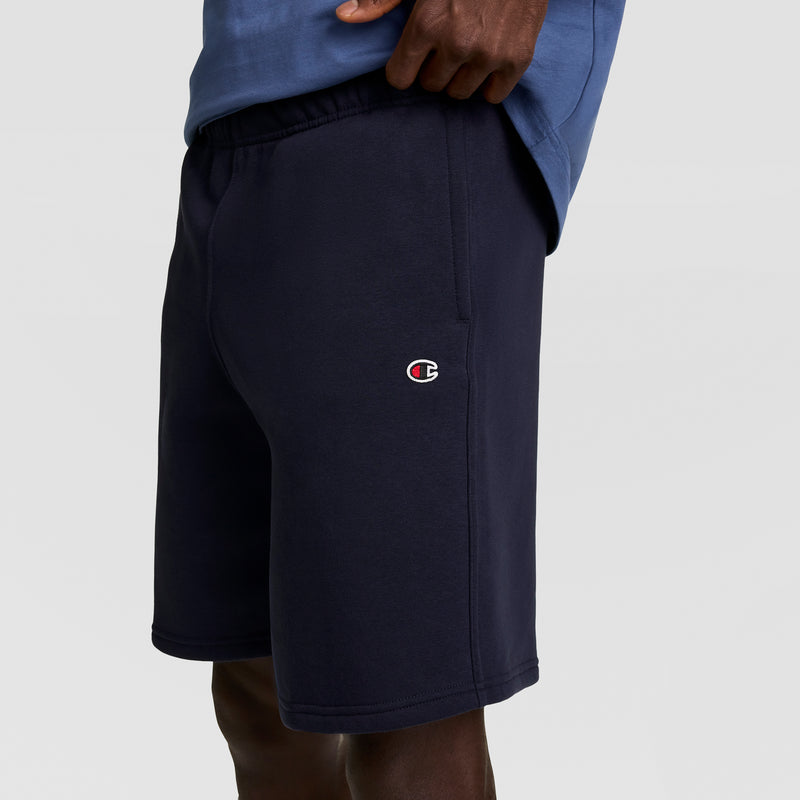 A person wearing navy blue Champion 10" Powerblend Fleece Shorts and a blue shirt, with only torso and legs visible against a plain background.