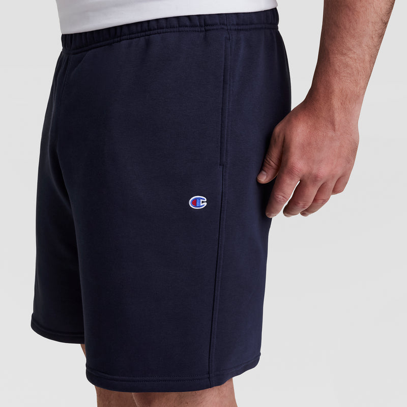 A person models the Champion 10" Powerblend Fleece Short - Big & Tall in navy blue with a small left leg logo, against a plain white background. Only their torso and upper legs are visible.