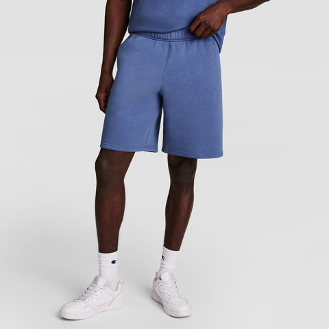 A person wearing Champion 10" Powerblend Fleece Shorts in blue, with a matching blue shirt, white socks, and white sneakers stands against a plain light gray background. The image focuses on the lower half of the body.