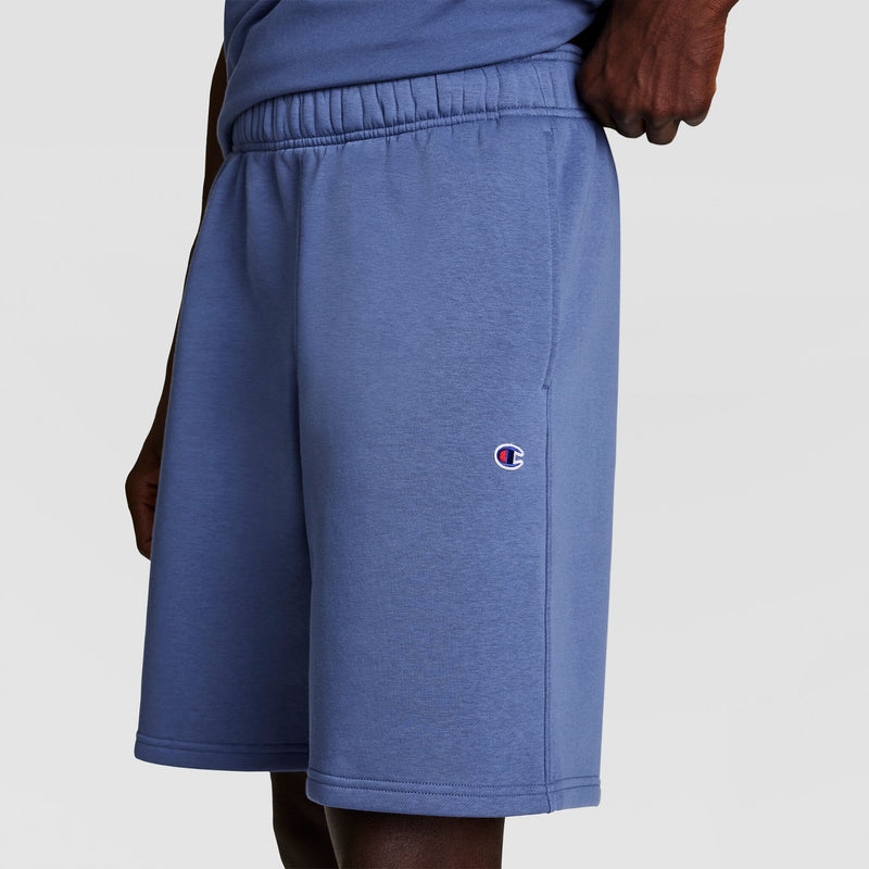 Someone wearing Champion 10" Powerblend Fleece Shorts in light blue, featuring an elastic waistband and the Champion logo on the left leg, stands against a plain background.