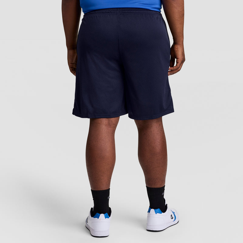 A person is shown from the back wearing Champion’s 9" Classic Mesh Shorts, C Logo - Big & Tall in navy blue, paired with a blue shirt, black socks, and white sneakers with blue accents against a plain light gray background.