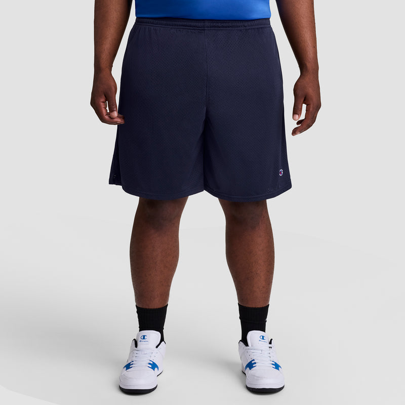 A person stands facing forward against a light gray background, showing only the lower half of their body. They are wearing Champion's 9" Classic Mesh Shorts, C Logo - Big & Tall, along with black socks and white sneakers.